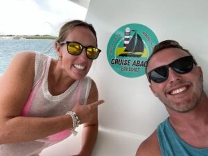 smiling couple pointing to logo of owner-operated cruise abacos sailing school and yacht charter