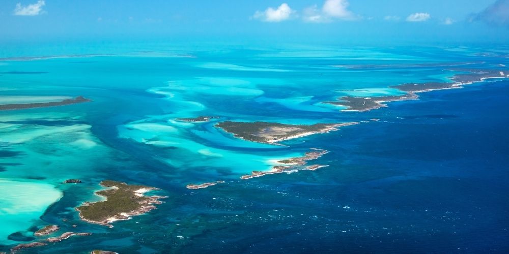 Aerial view of turquoise lagoons and small islands along a bright blue ocean coastline.